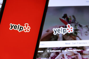 Mobile phone with Yelp icon on full screen close up with website on laptop.