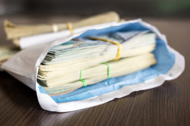 Bundle of american dollar banknotes in white envelope on wooden table.