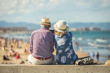 Mature couple of retired lovers enjoying retirement on the beach facing the sea with mobile cell phone taking pictures at sunset.