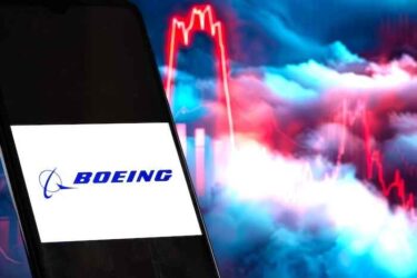Logo of Boeing is sharp in the foreground, while the stock chart in the clouds is blurred in the background