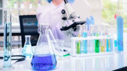 Blue solution in flask and measuring cylinder and the laboratory glassware was placed in the front of Scientists are experimenting and examining specimens with microscopes in the lab.
