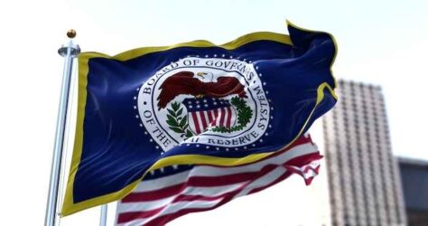 The flag of the American Federal Reserve System waving in the wind with the flag of the United States blurred in the background.