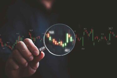 Trader hand holding magnifier glass with stock market for analysis technical graph of stock market chart