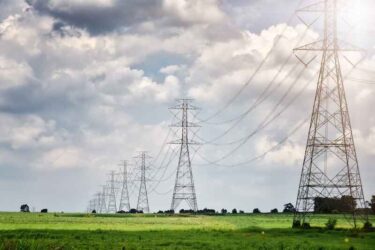 High voltage tower, Electric post and electric cable on the field in the countryside with white cloudy and blue sky background.