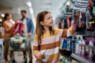 Smiling little girl buying school supplies while being with her parents in a bookstore.