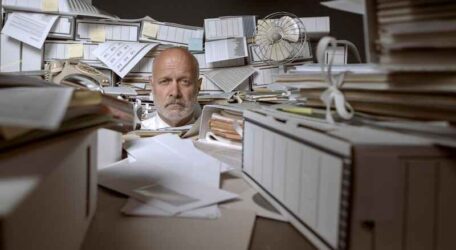 Disappointed stressed businessman overwhelmed by paperwork, he is stressed and looking at camera