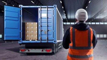 Truck with container. Man logistician with his back to camera. Truck inside industrial hangar. Pallets with boxes delivered to warehouse.